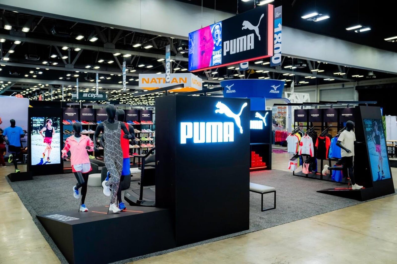 LED tower booth with an illuminated logo block and mannequin display platforms on a convention floor