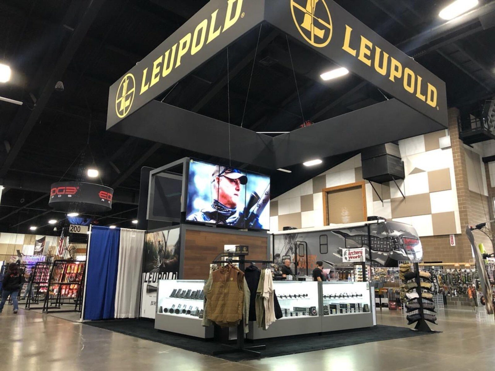 Island booth with a suspended square sign ring over lit product cases and an open counter