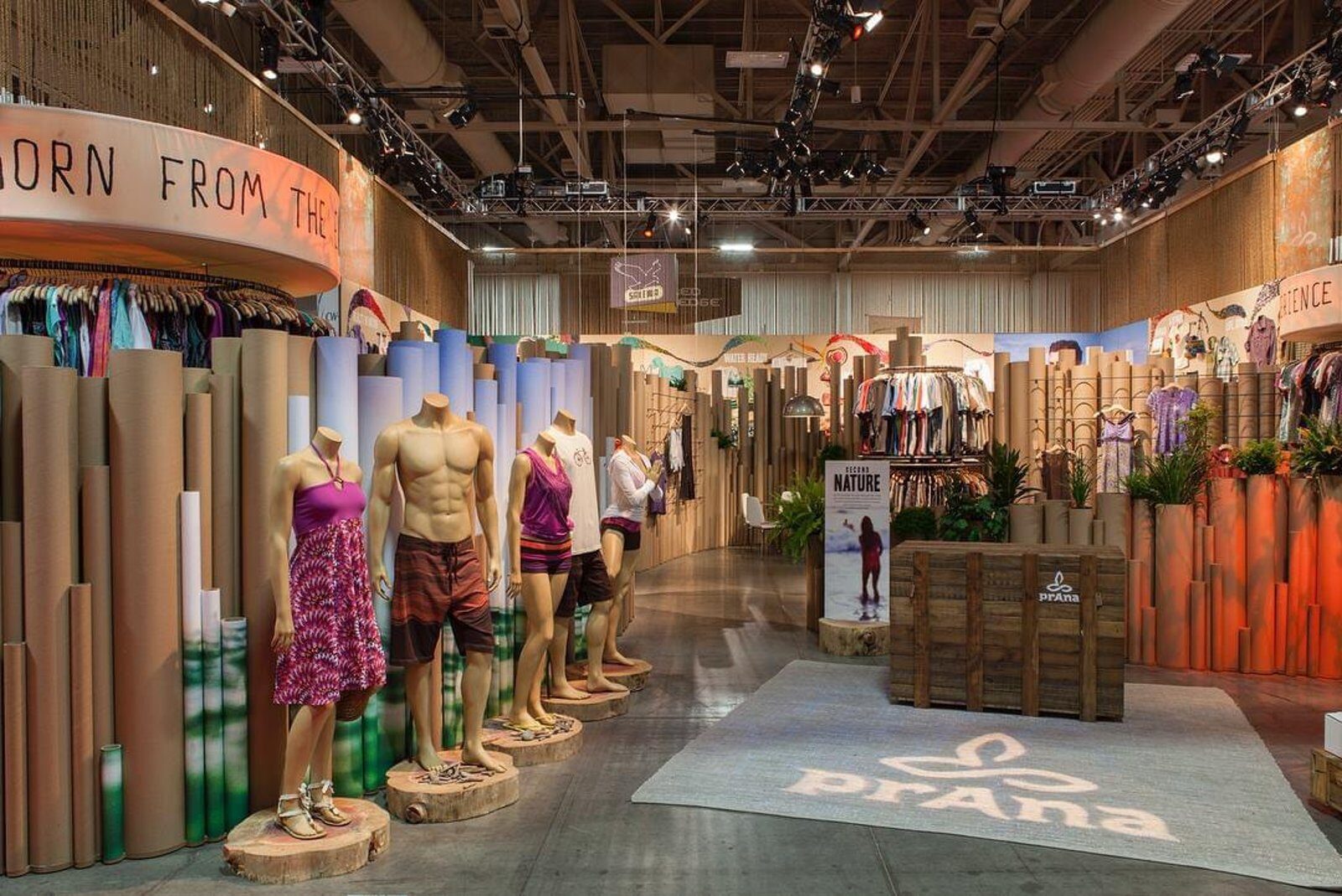 Two-level exhibit built from stacked cardboard tubes with an elevated brand ring and mannequin displays